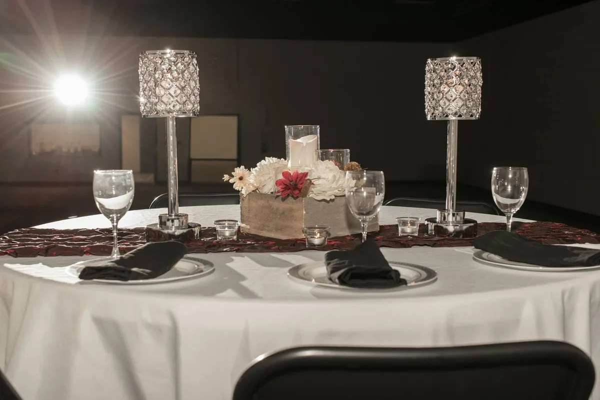 A round guest table dressed with linens, candle lamps, and a floral centerpiece